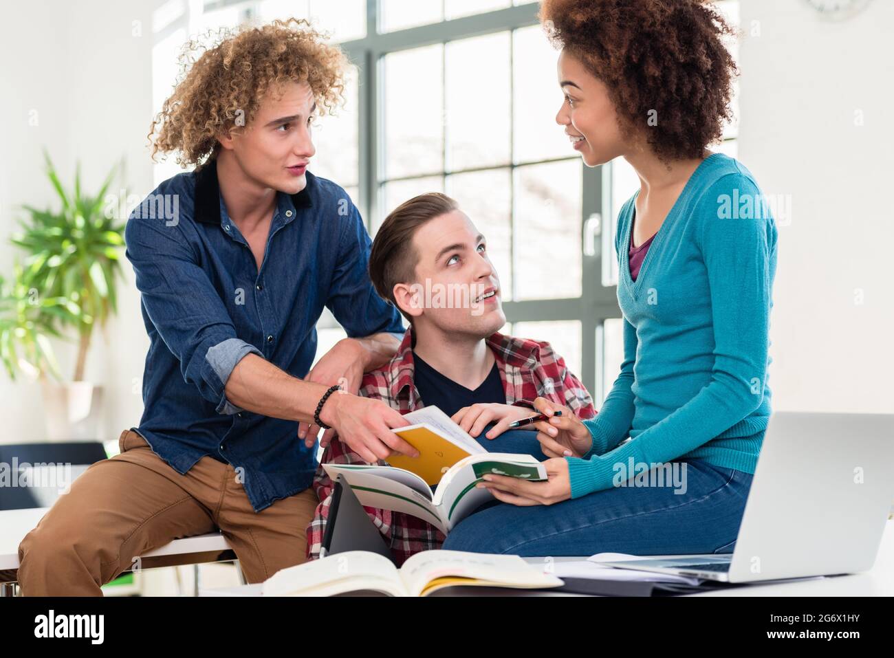 Three students sharing ideas and opinions while comparing information from two different textbooks during break at college Stock Photo