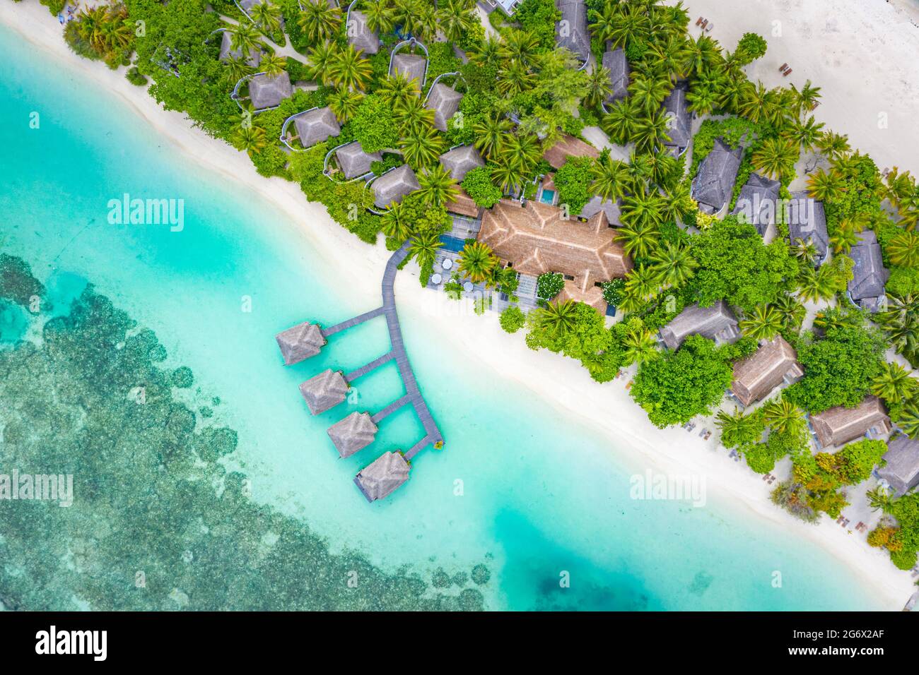 Aerial landscape from drone view blue water and wooden bridge and water villas with paradise island shore, sea coast palm tree. Stunning aerial travel Stock Photo