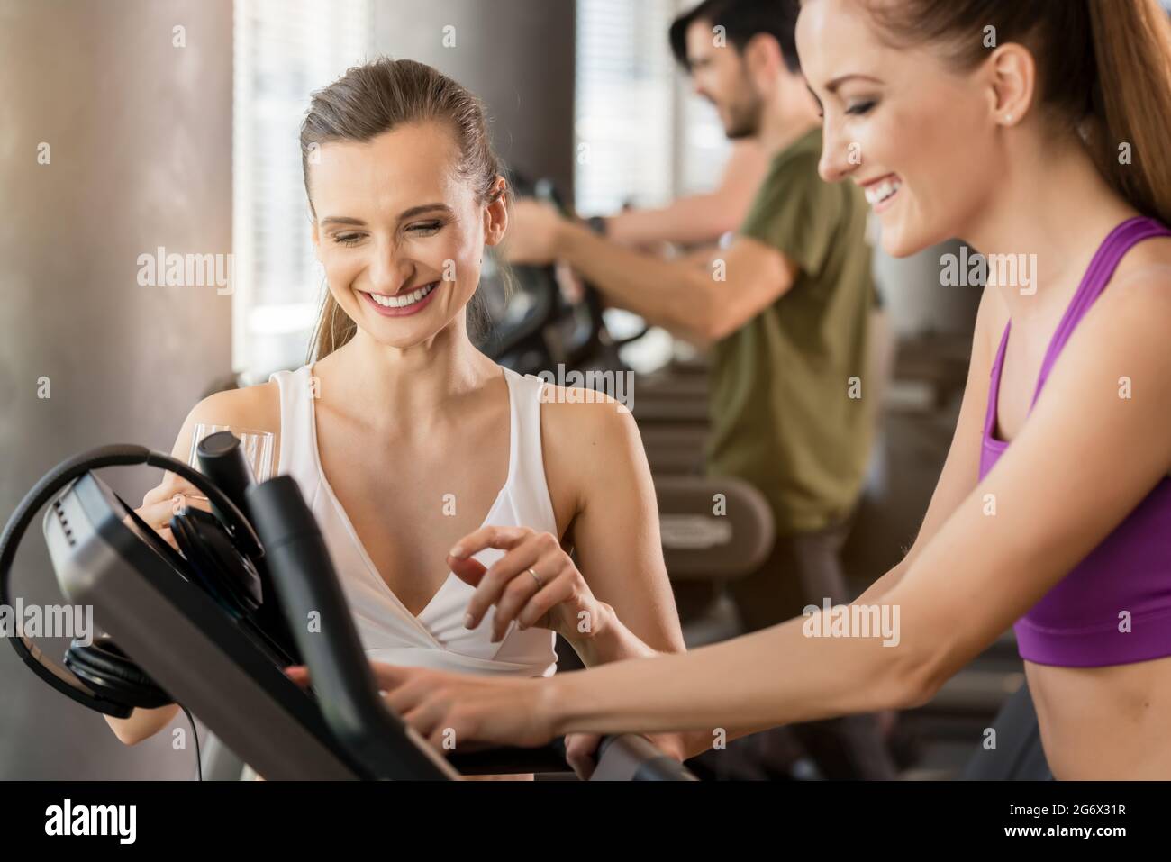 Young woman helping her friend to set the time, speed and incline of ...