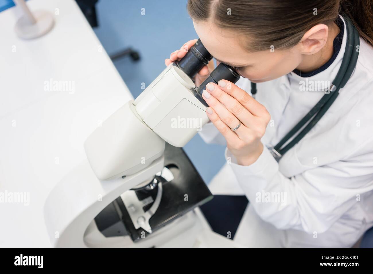 Doctor or biologist with stethoscope scrutinizing tissue under microscope Stock Photo
