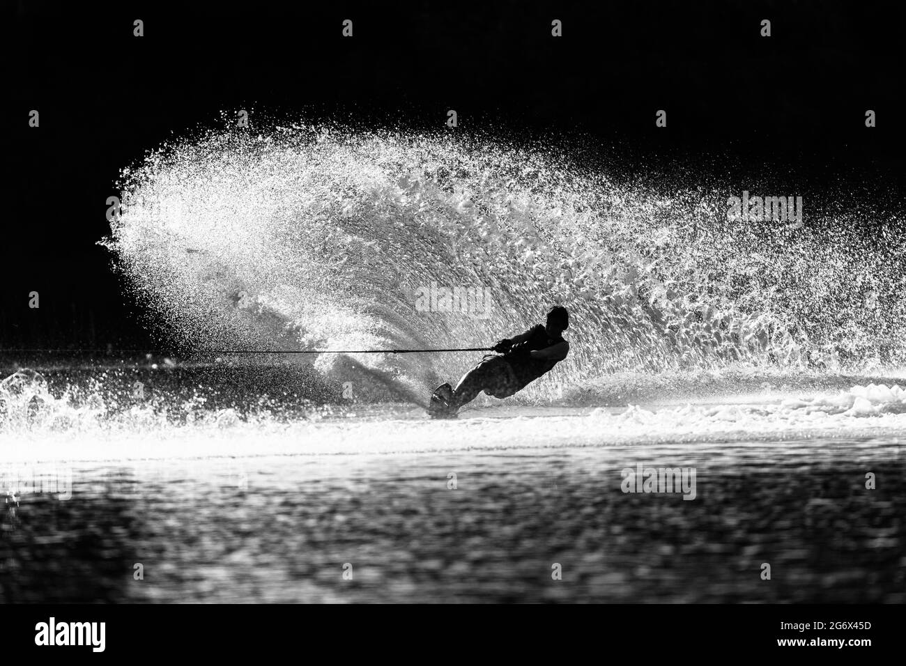 Water ski young Man unrecognizable athlete skiing slalom carves a vertical water wake spray  in vintage sepia black white tone for a dramatic contrasts Stock Photo