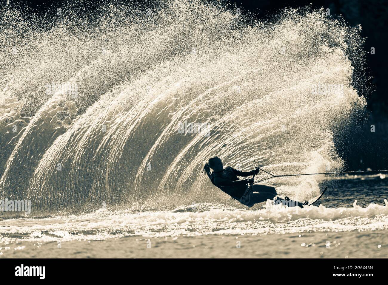 Water ski girl unrecognizable athlete skiing slalom carves a vertical water wake spray  in vintage sepia black white tone for a dramatic contrasts. Stock Photo