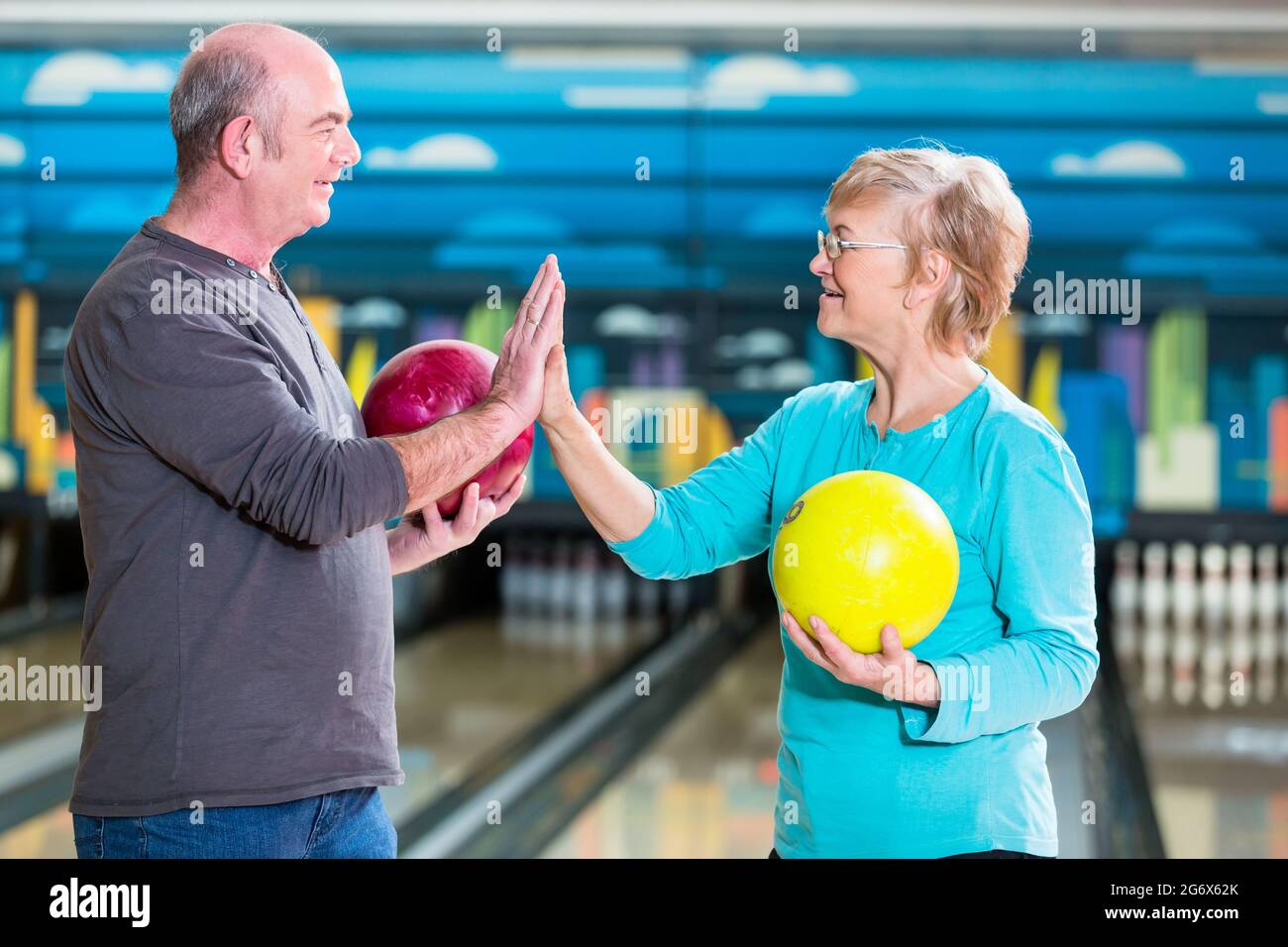 Smiling mature couple holding bowling ball giving high-five Stock Photo