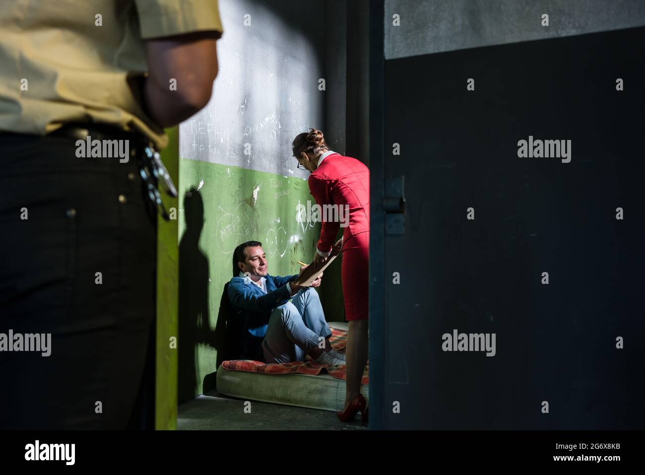 Dedicated female attorney visiting a young male inmate while helping him with the legal procedures in an obsolete prison cell during custody Stock Photo