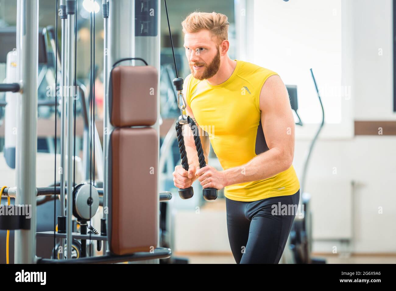 Handsome and determined bodybuilder exercising triceps pushdown at the rope cable machine during