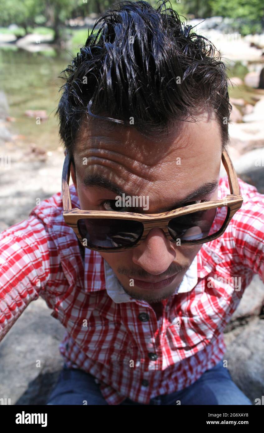 Man with dark wet hair looking over his sunglasses in a skeptical way Stock Photo