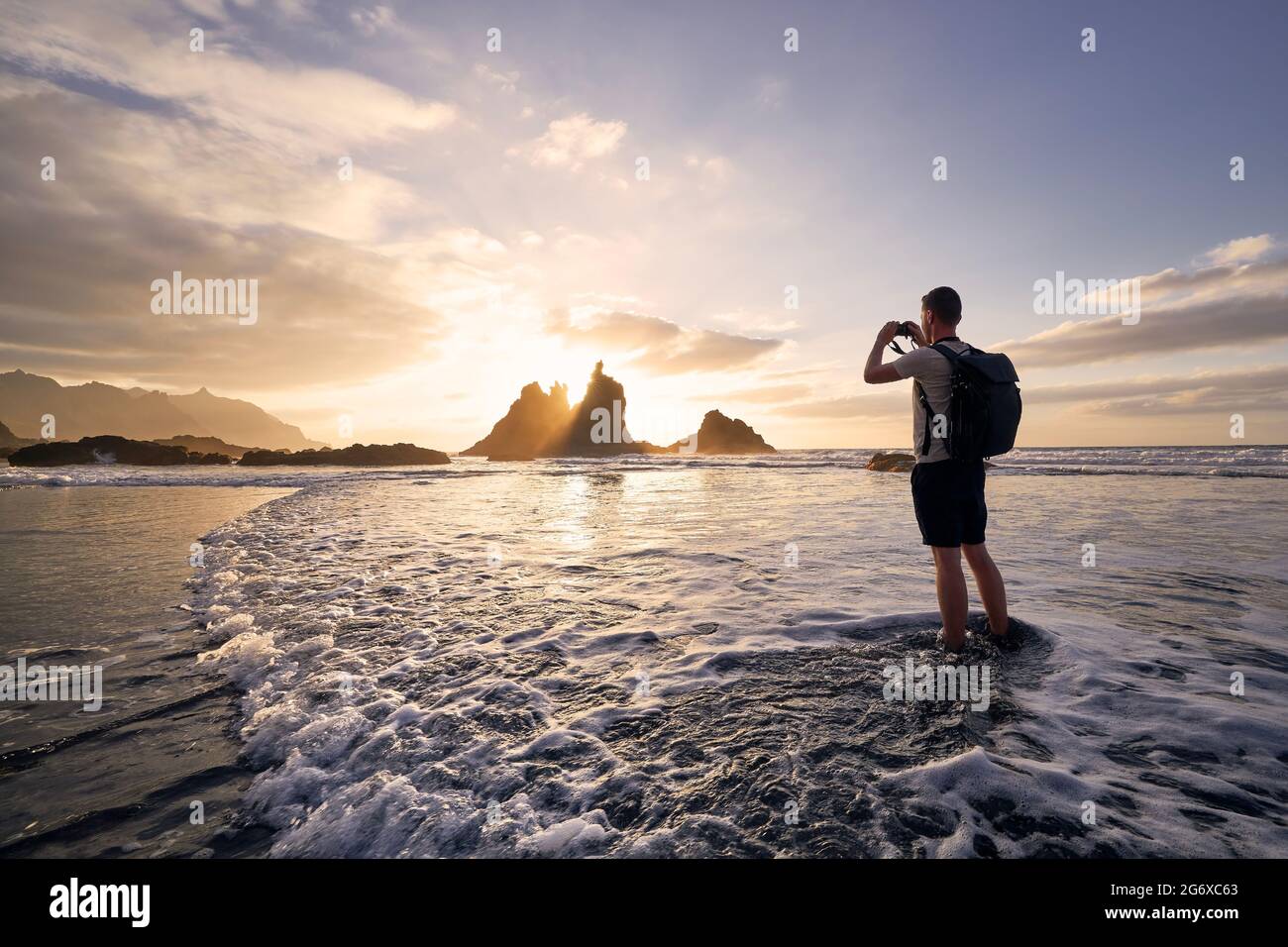 Man during photographing landscape with cliff. Young photographer on beach at beautiful sunset. Tenerife, Canary Islands, Spain. Stock Photo