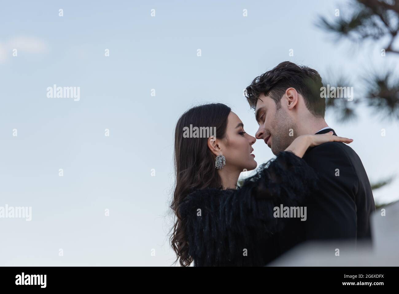 side view of man and woman in faux fur jacket hugging against blue sky ...