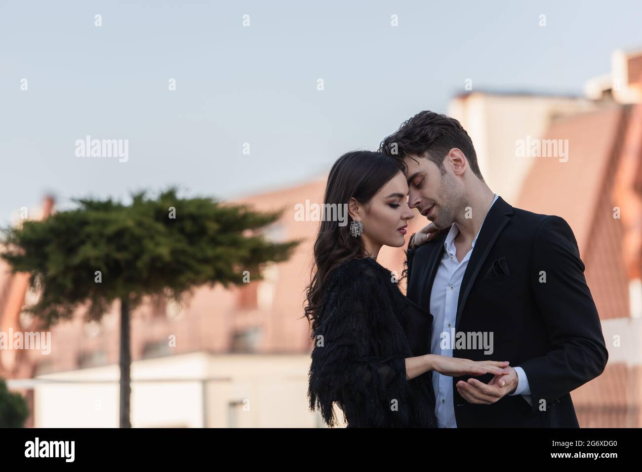 man hugging woman in dress and faux fur jacket on terrace of restaurant ...