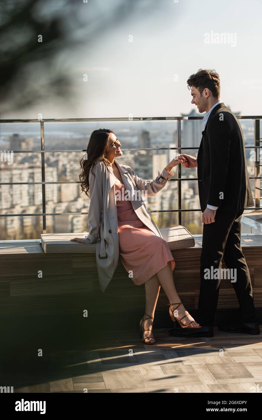 happy woman in dress and coat sitting and holding hands with man in ...
