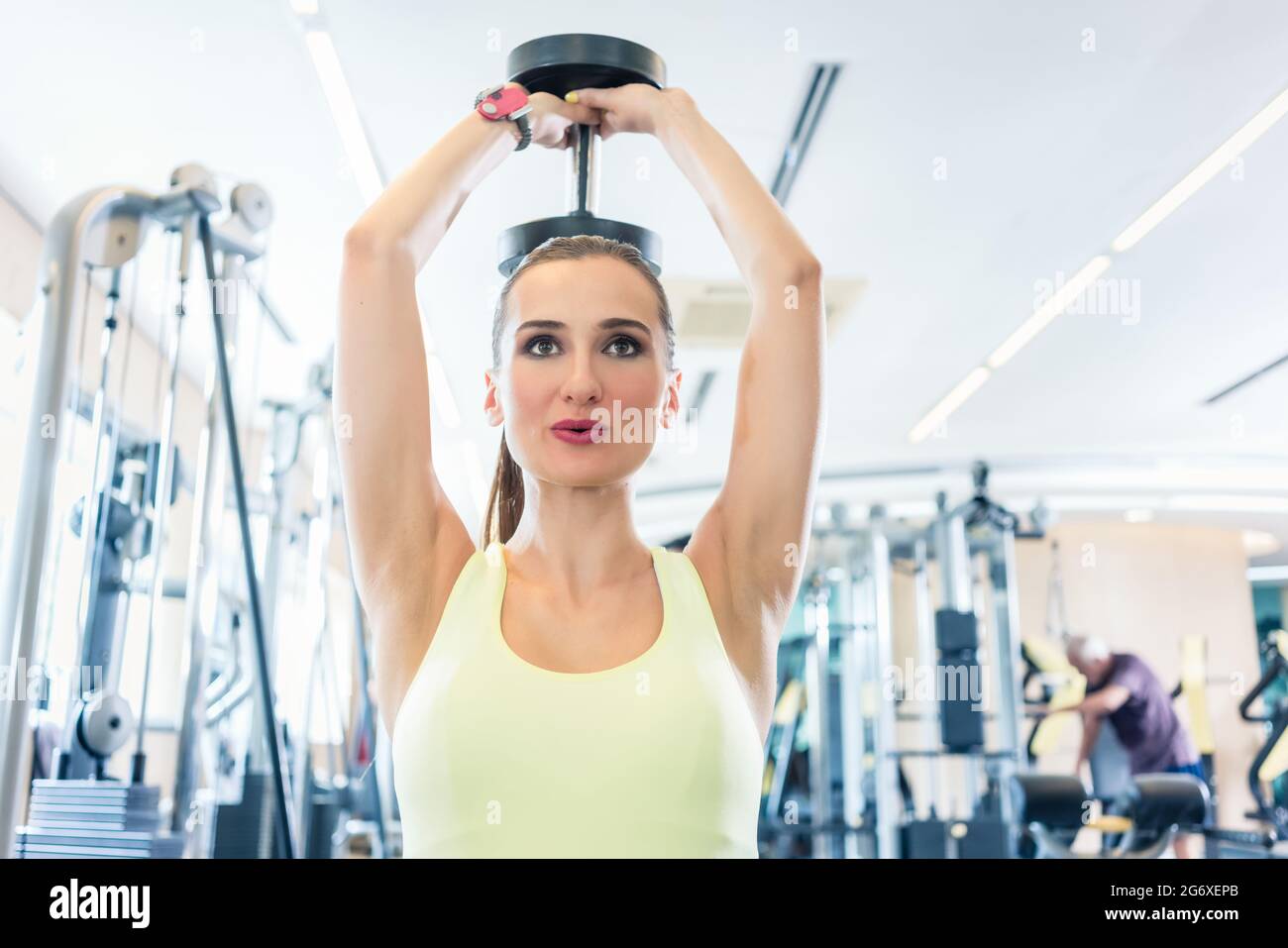 Portrait of a beautiful fit woman with can do attitude exercising triceps extension with dumbbell during workout in a modern fitness club Stock Photo