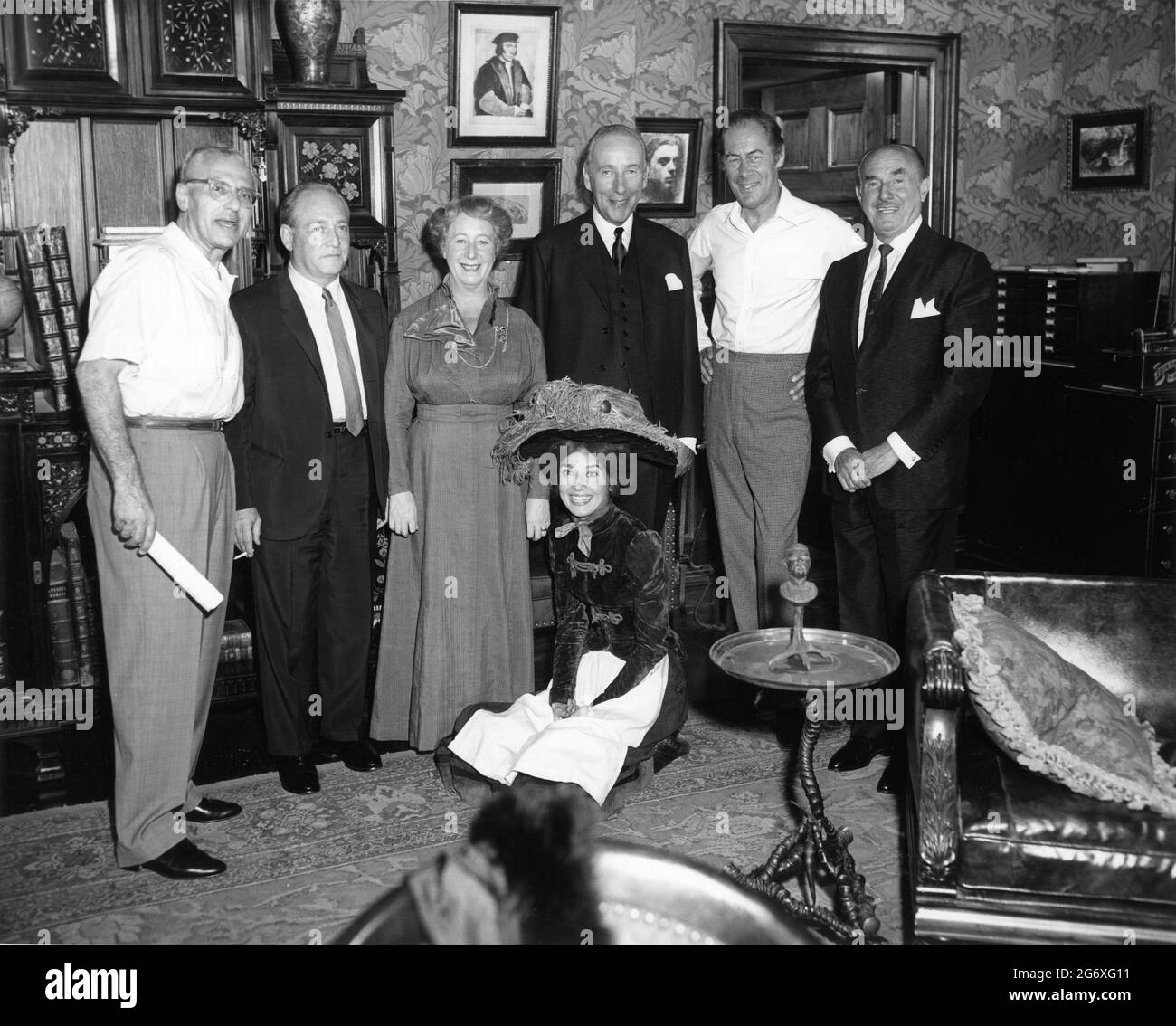Director GEORGE CUKOR, Warners Vice President STEPHEN B. TRILLING, MONA WASHBOURNE, WILFRID HYDE-WHITE, REX HARRISON Warners President JACK L. WARNER and AUDREY HEPBURN on set candid group photo during filming of MY FAIR LADY 1964 director GEORGE CUKOR from the Broadway musical adapted from the play Pygmalion by George Bernard Shaw screenplay book and lyrics Alan Jay Lerner music Frederick Loewe production design and costumes Cecil Beaton producer Jack L. Warner Warner Bros. Stock Photo