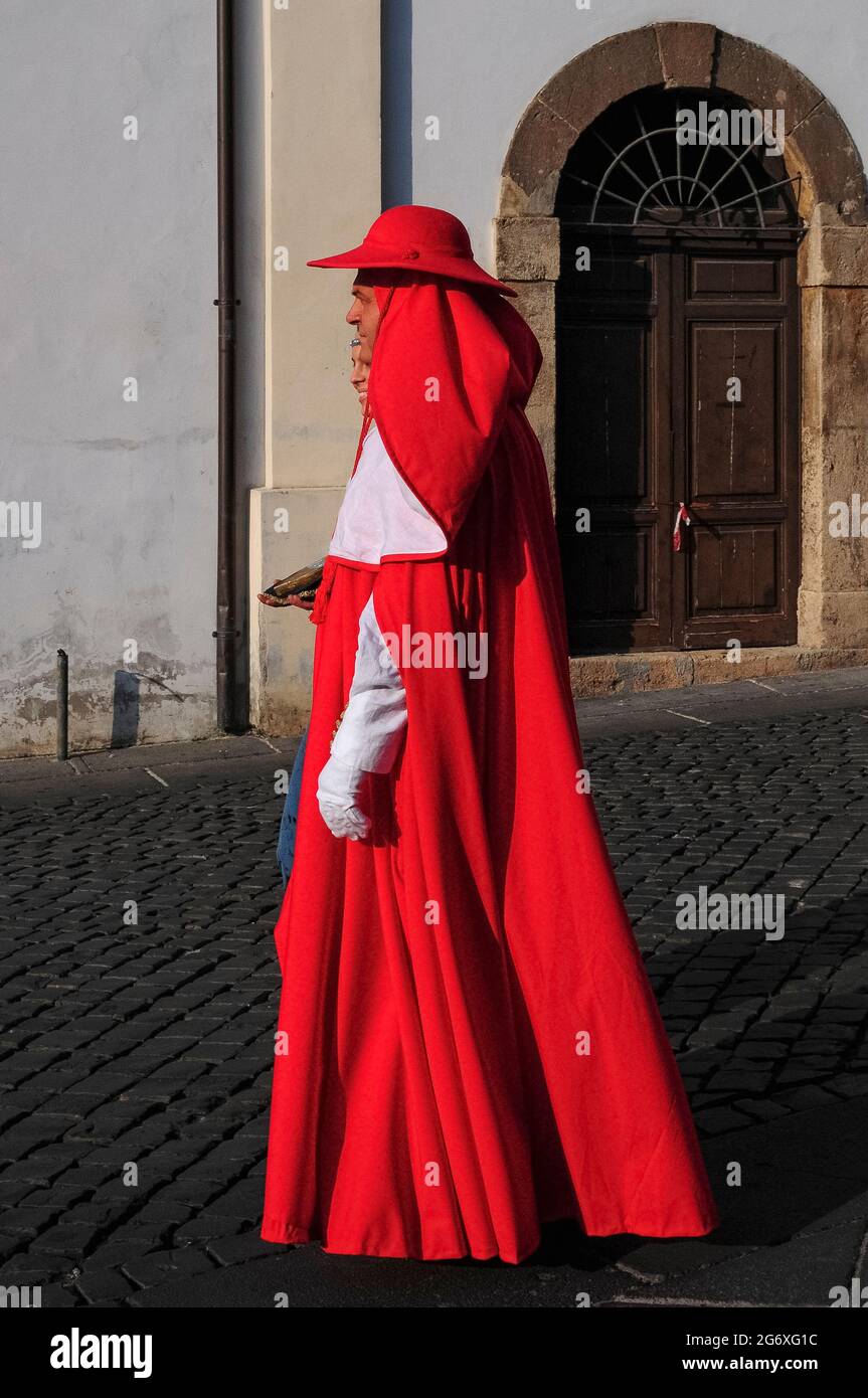 A man wearing a splendid red and white cardinal costume strolls with a finely-dressed lady through Piazza Guglielmo Marconi in Anagni, Lazio, Italy, in an historical August pageant recalling its past as City of the Popes, the summer retreat between the 11th and 14th centuries of pontiffs who preferred its relative cool to the sweltering heat of Rome.  Anagni was also the birthplace of popes Gregory IX and Boniface VIII. Stock Photo