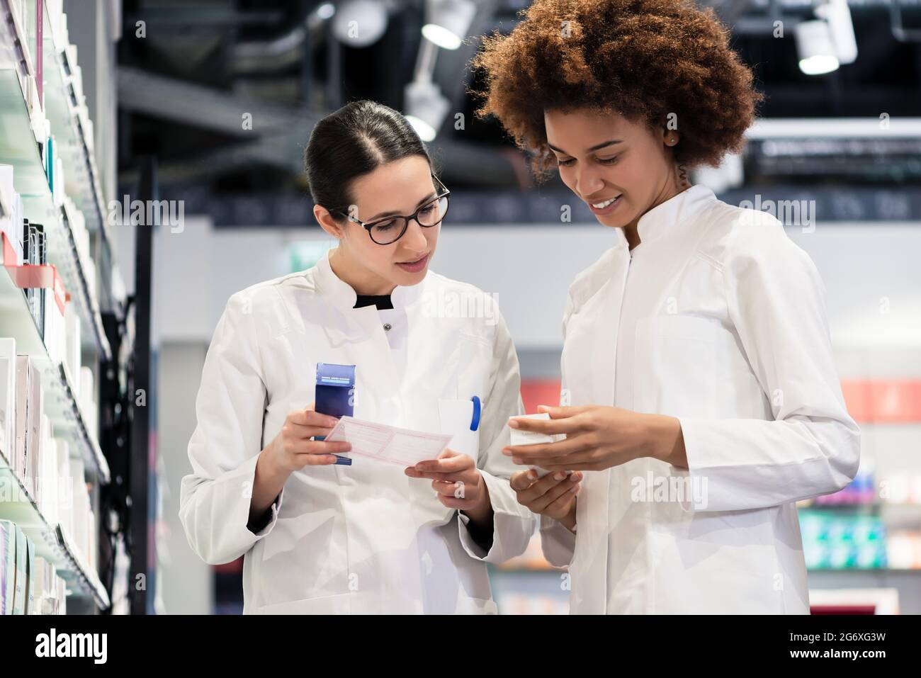 Low-angle view of two reliable pharmacists analyzing together a medical prescription and two different packages of medicine during work in a modern dr Stock Photo