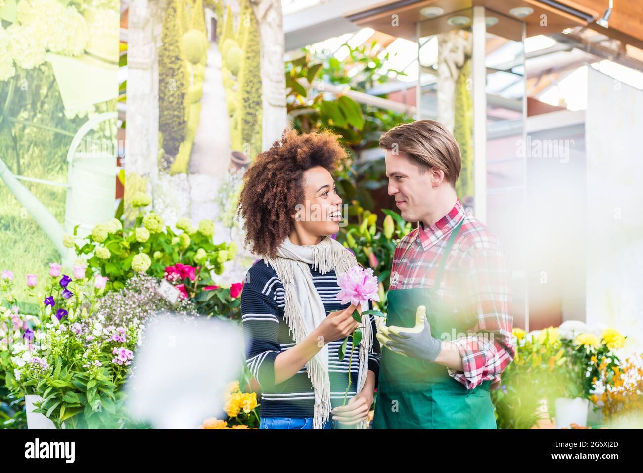 Cheerful Latin American female customer buying flowers at the advice of a helpful and persuasive vendor in a modern flower shop Stock Photo