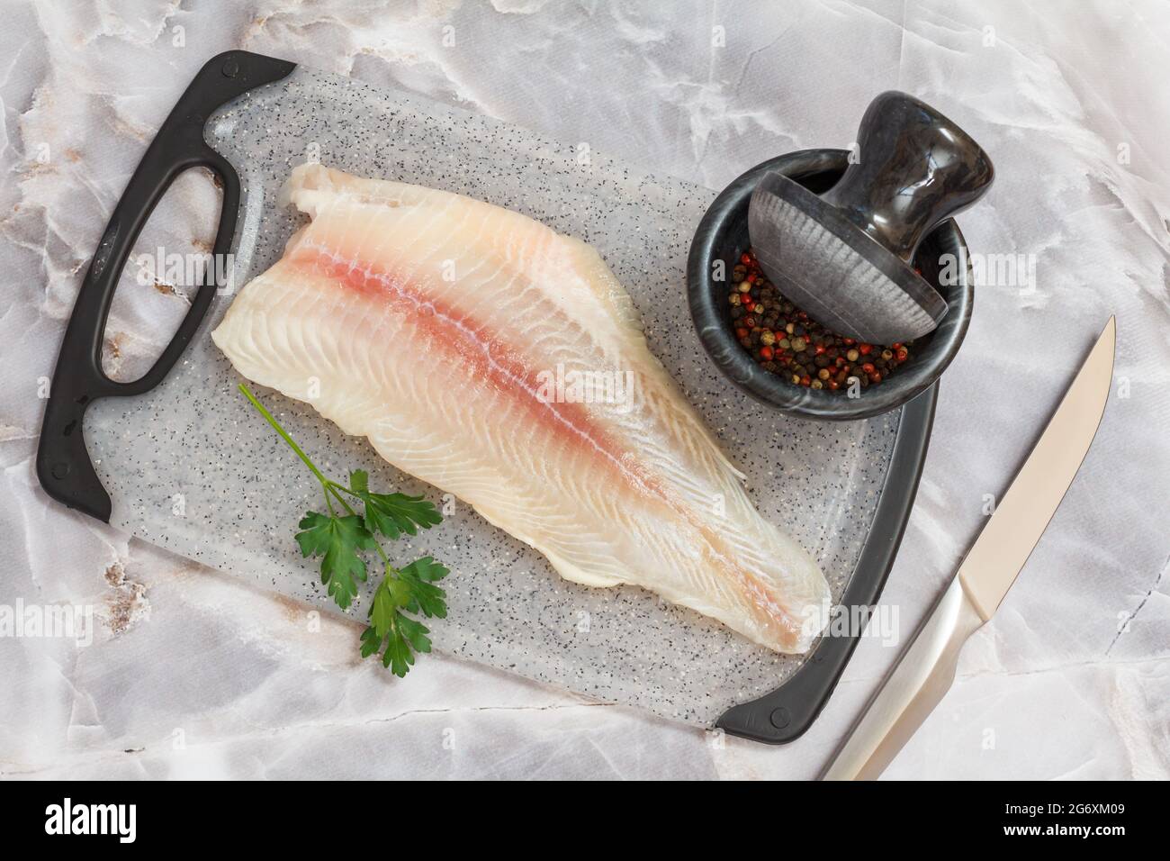 Fillet of raw pangasius fish with parsley on cutting board Stock Photo