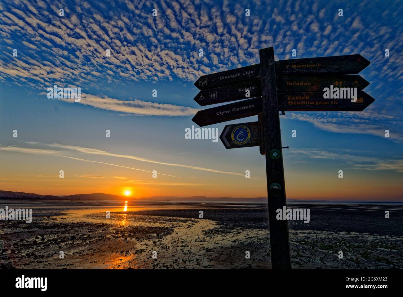 Wooden direction signs by the promenade in West Cross, as the sun rises marking the beginning of the meteorological summer, Swansea Bay, Wales, UK. Tu Stock Photo