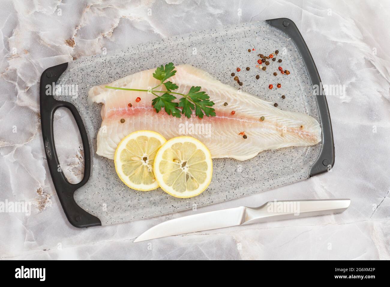 Fillet of raw pangasius fish with parsley leaves and lemon on cutting board Stock Photo