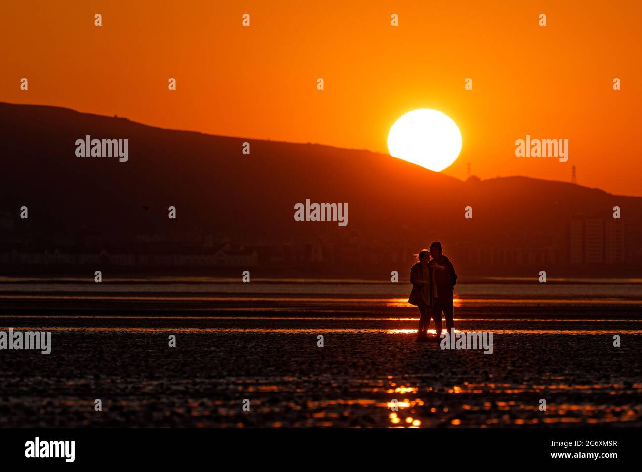 A young couple take a selfie on the beach as the sun rises, marking the beginning of the meteorological summer, Swansea Bay, Wales, UK. Tuesday 01 Jun Stock Photo