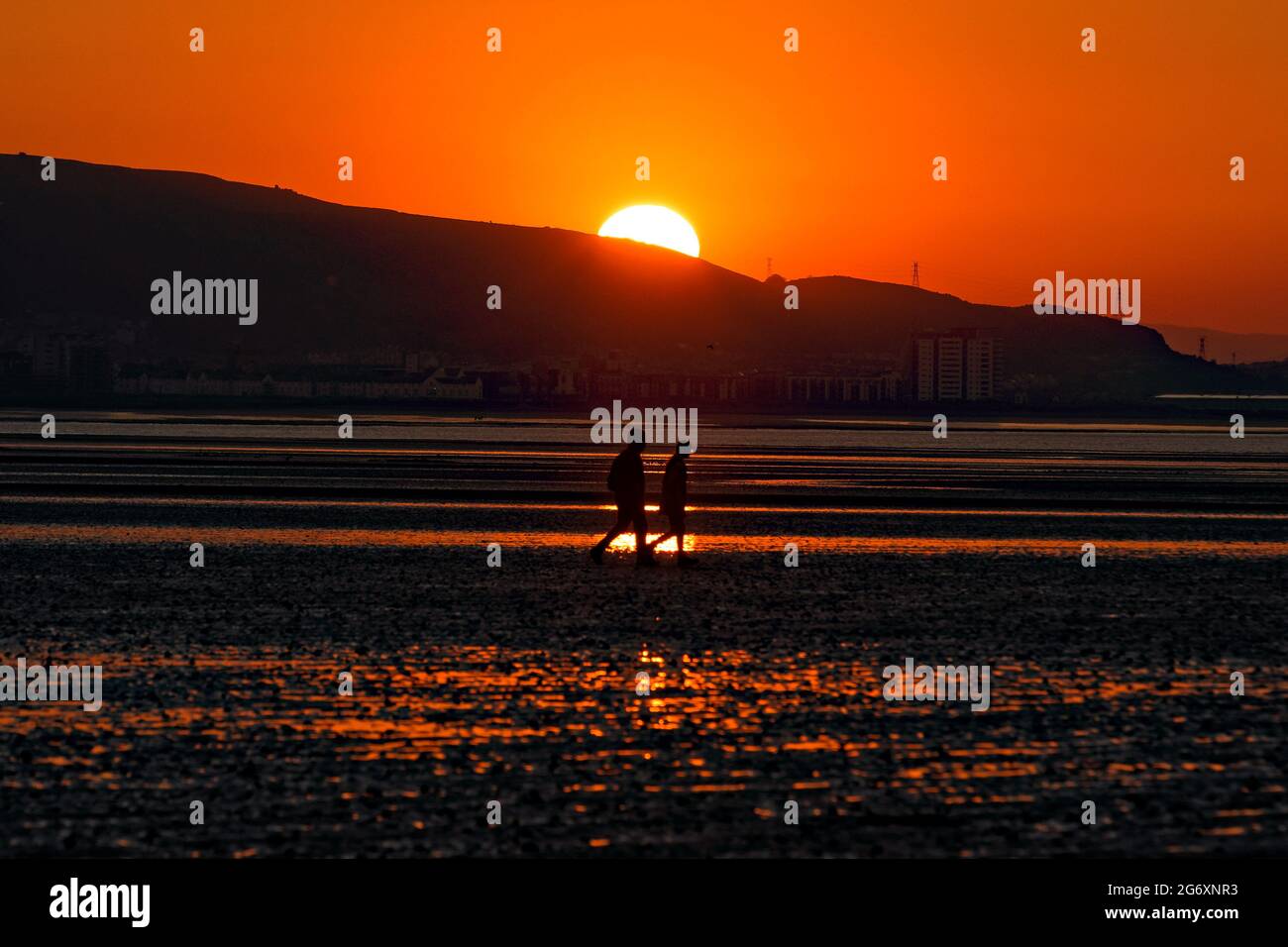 A young couple walk on the beach as the sun is about to rise, marking the beginning of the meteorological summer, Swansea Bay, Wales, UK. Tuesday 01 J Stock Photo