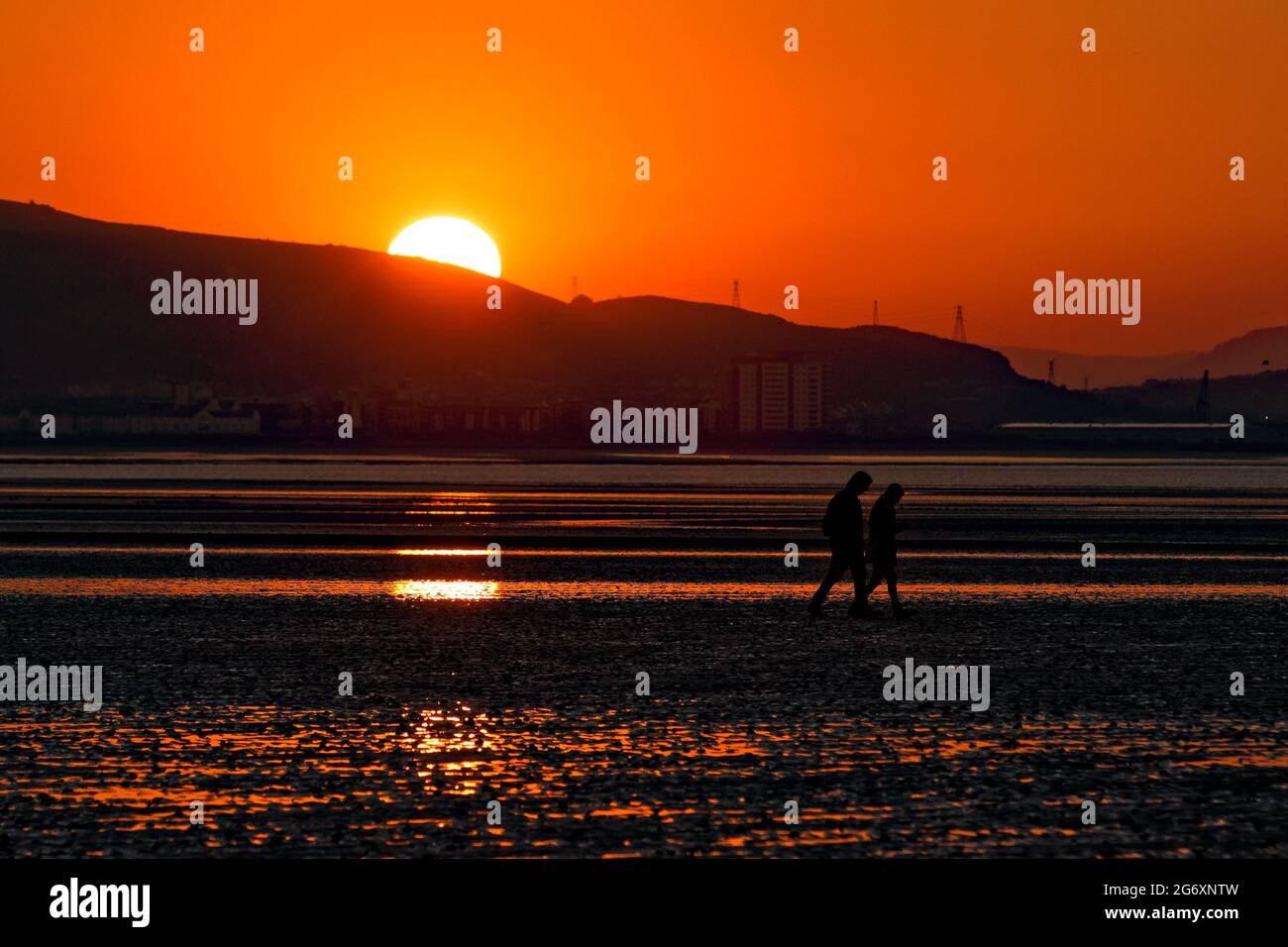 A young couple walk on the beach as the sun is about to rise, marking the beginning of the meteorological summer, Swansea Bay, Wales, UK. Tuesday 01 J Stock Photo