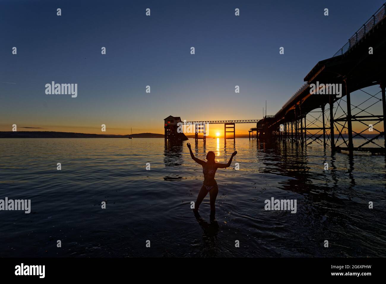 Pictured: Natasha Jenkins in the sea during sunrise as seen through the RNLI boat station in Mumbles, near Swansea, Wales, UK. Sunday 13 June 2021 Re: Stock Photo