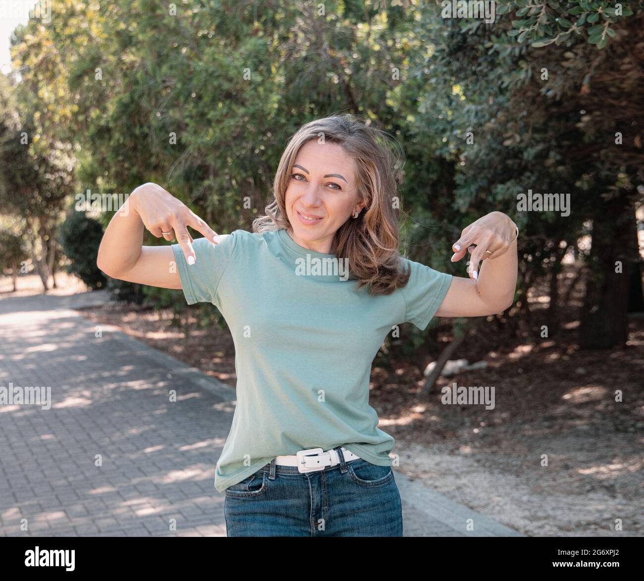 Middle aged women wearing t-shirt and jeans pointing on t-shirt stays outdoor in the park Stock Photo