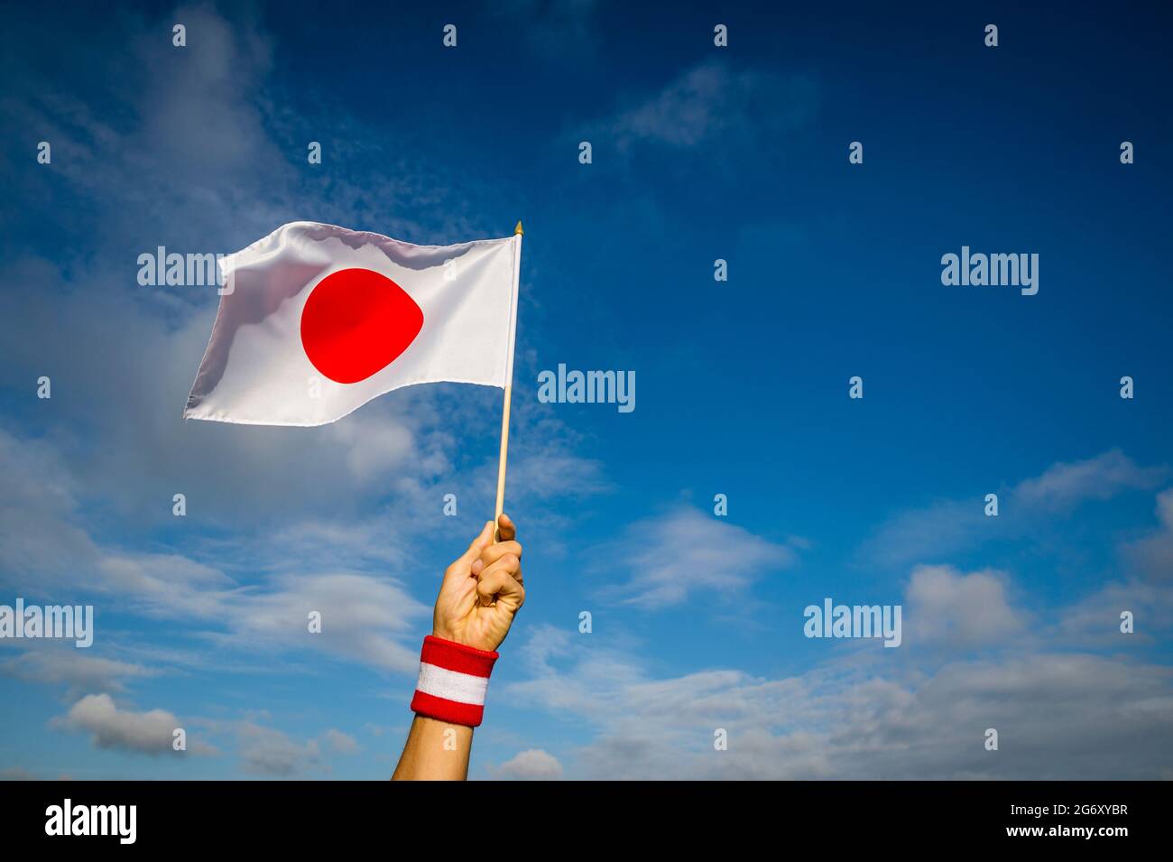 Japanese athlete with red and white wristband proudly holding national flag of Japan waving in bright sunny blue sky Stock Photo