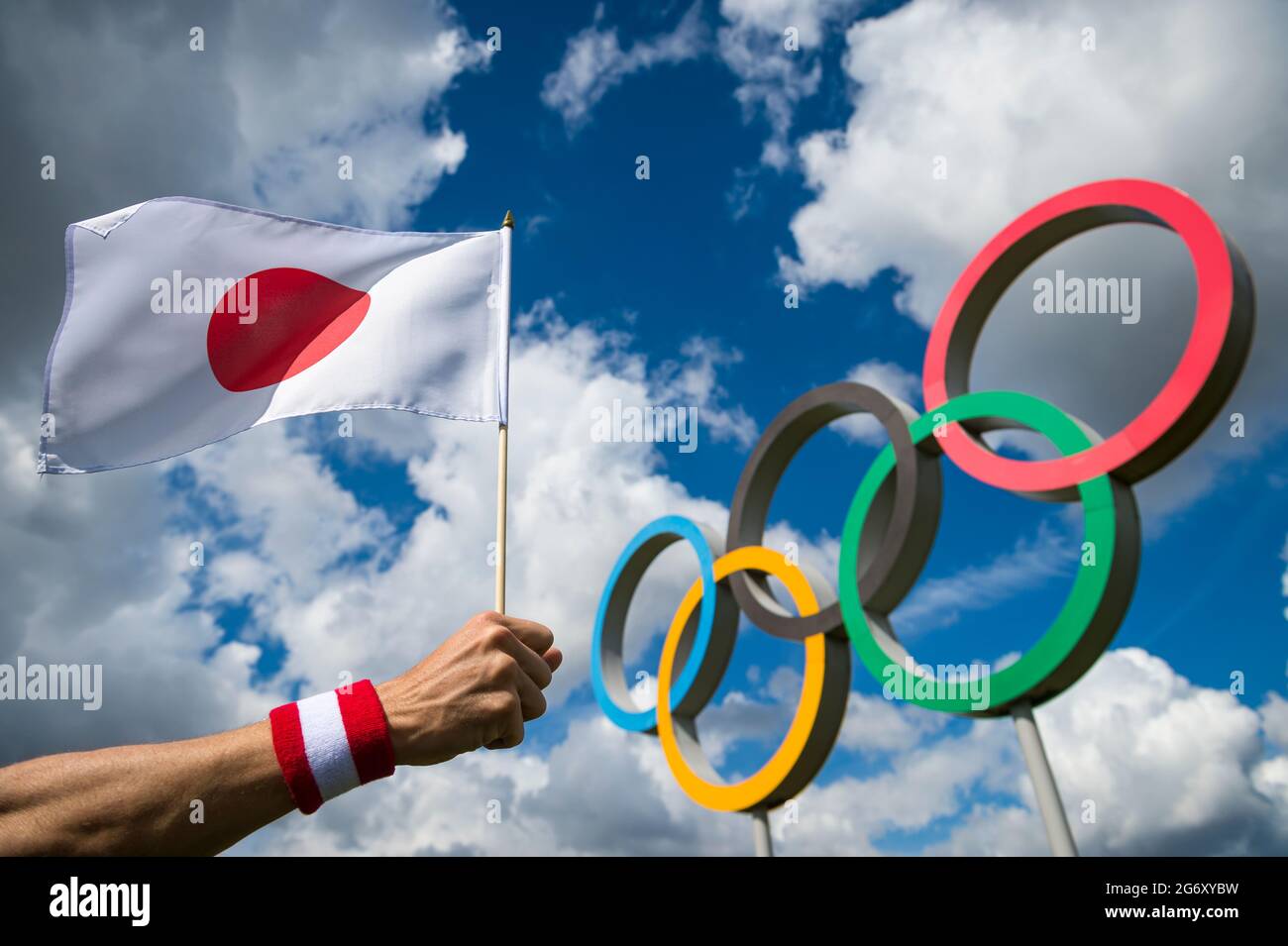 RIO DE JANEIRO - APRIL, 2016: A hand of Japanese athlete wearing a red and white wristband waves a Japanese flag in front of Olympic Rings and blue sk Stock Photo