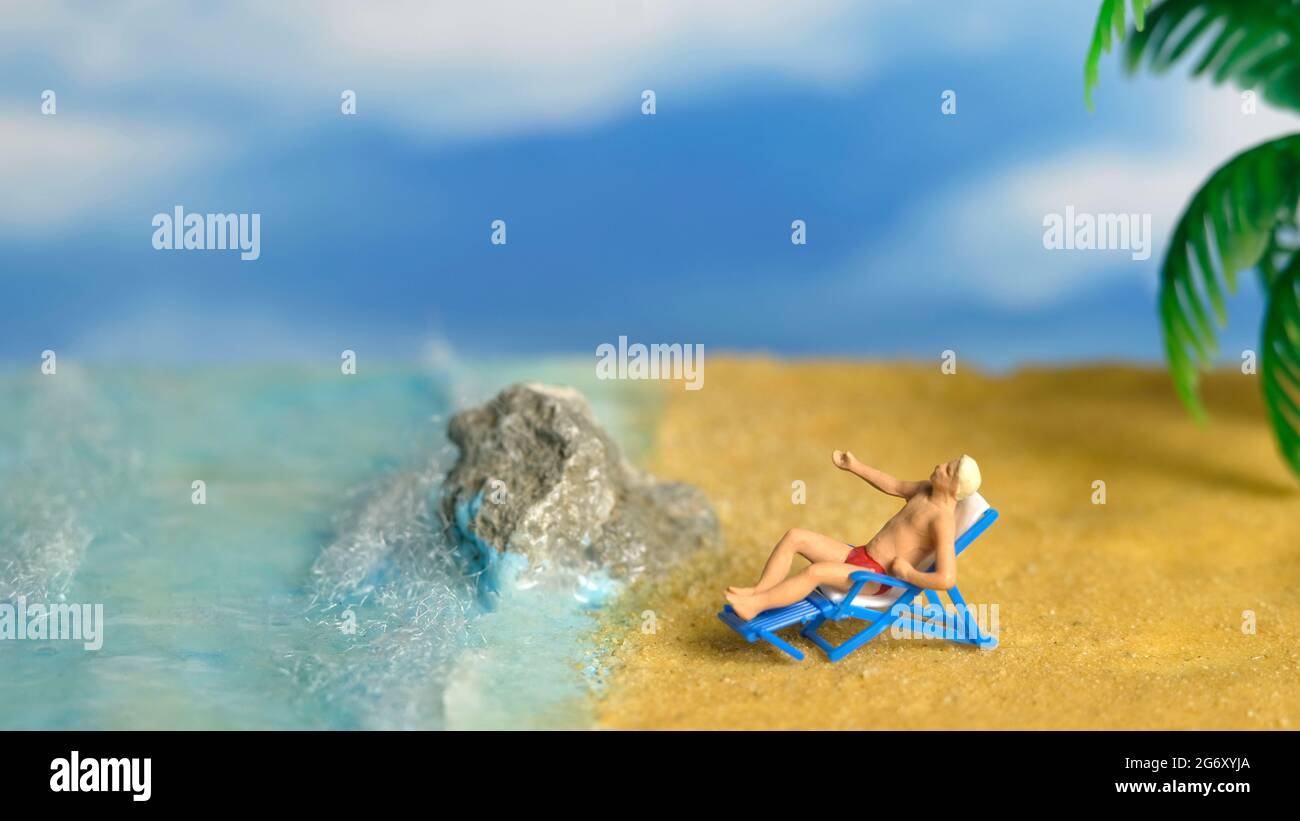 Miniature people toy figure photography. A Men relaxing on beach chair when daylight at seaside. Image photo Stock Photo