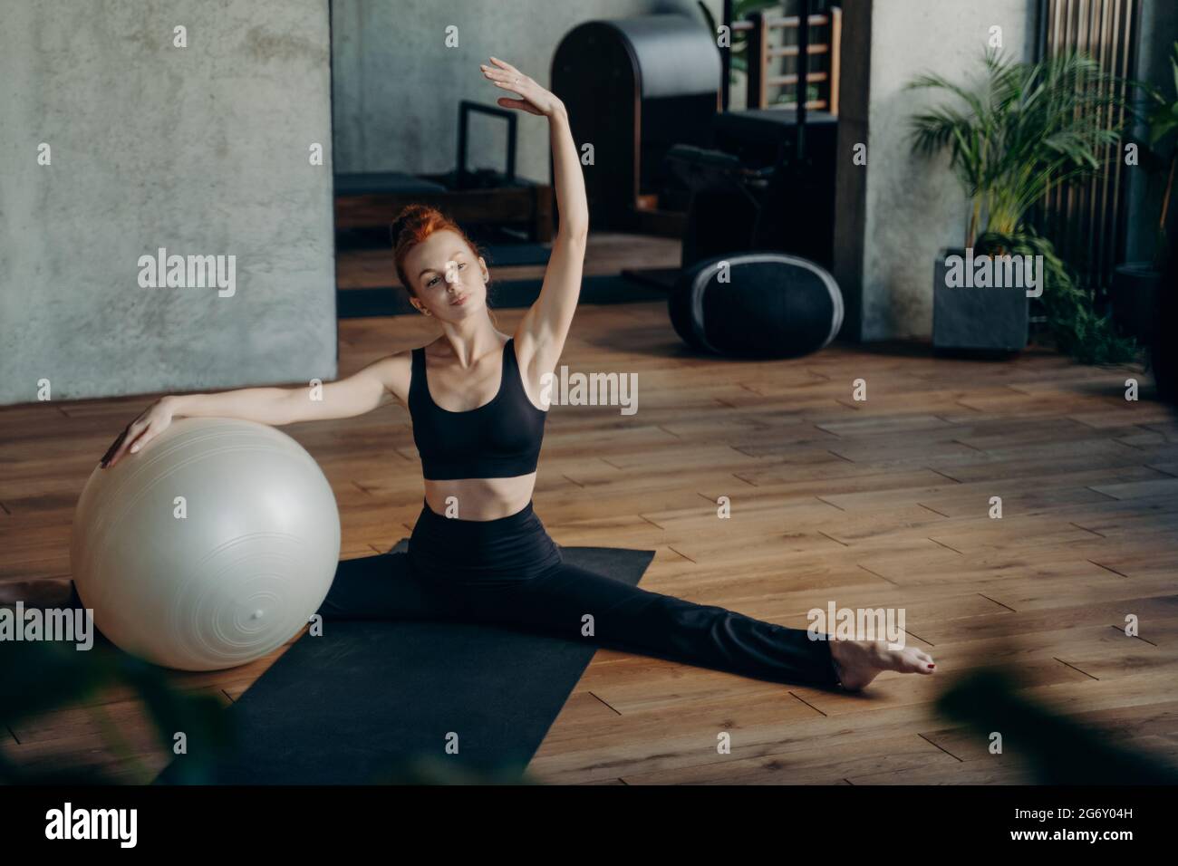 Young girl sitting in split position during pilates workout Stock Photo