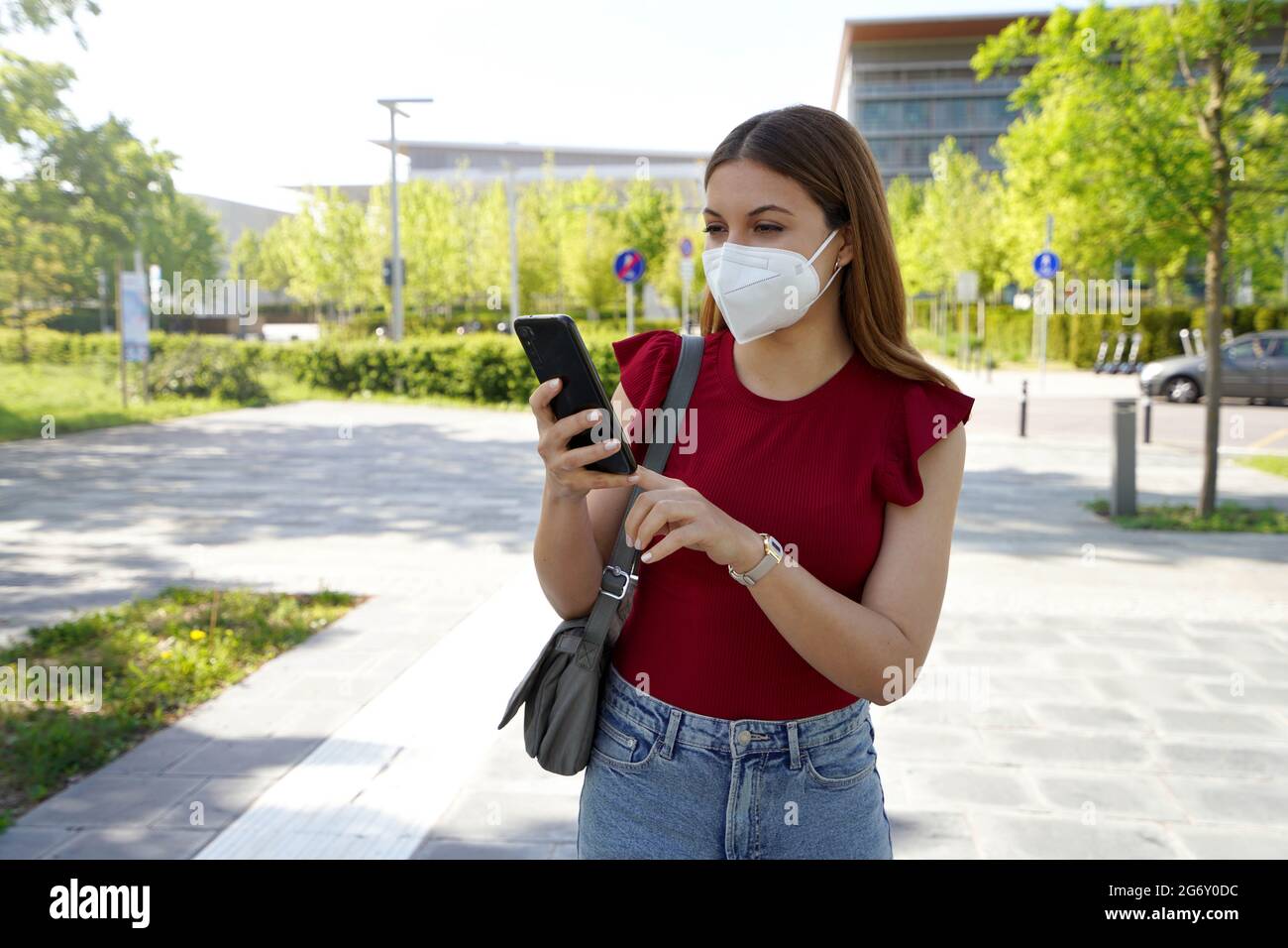 Happy young woman wearing FFP2 KN95 face mask on city street holding ...