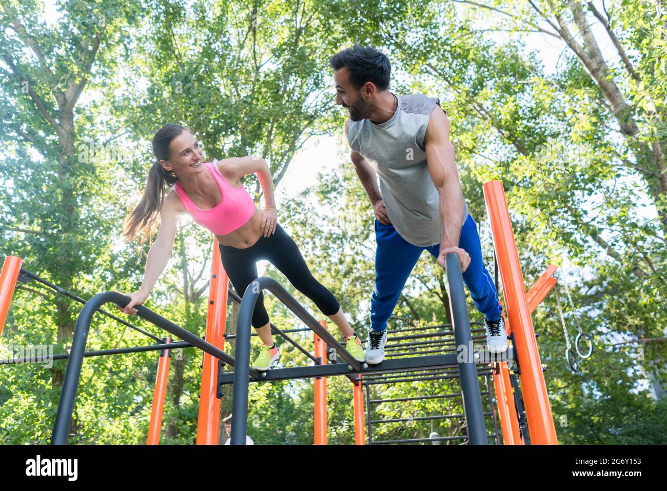 Low-angle view of a young fit woman and her partner smiling while practicing plank exercise during outdoor couple workout in a calisthenics park Stock Photo