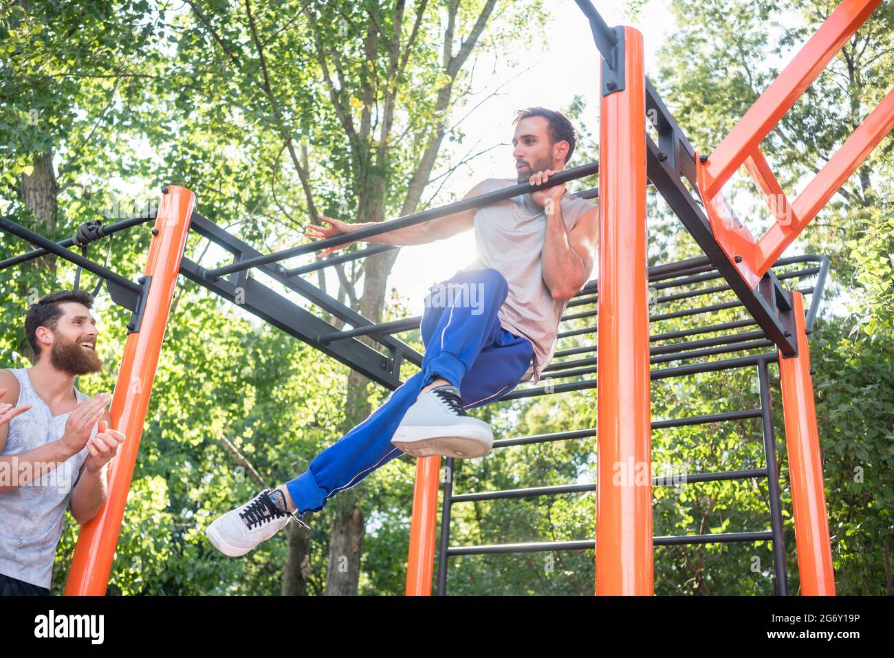 Low-angle view of a strong and determined young man doing amazing pull-up variation during extreme outdoor workout in the applauses of his friends Stock Photo