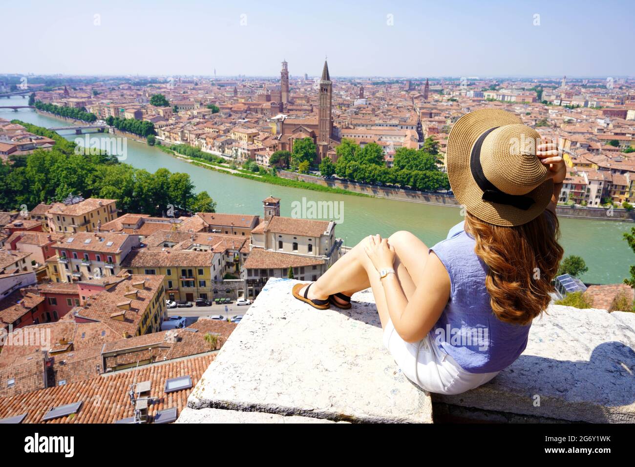Travel destination Italy. Wide angle from belvedere of young woman sitting on wall enjoying stunning view of Verona, Italy. Stock Photo