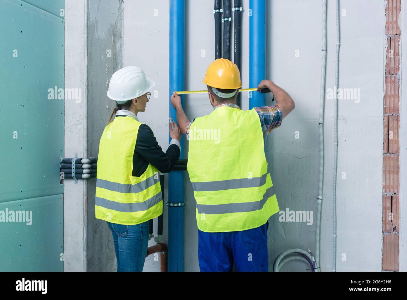 Construction workers measuring pipes on site with tape Stock Photo