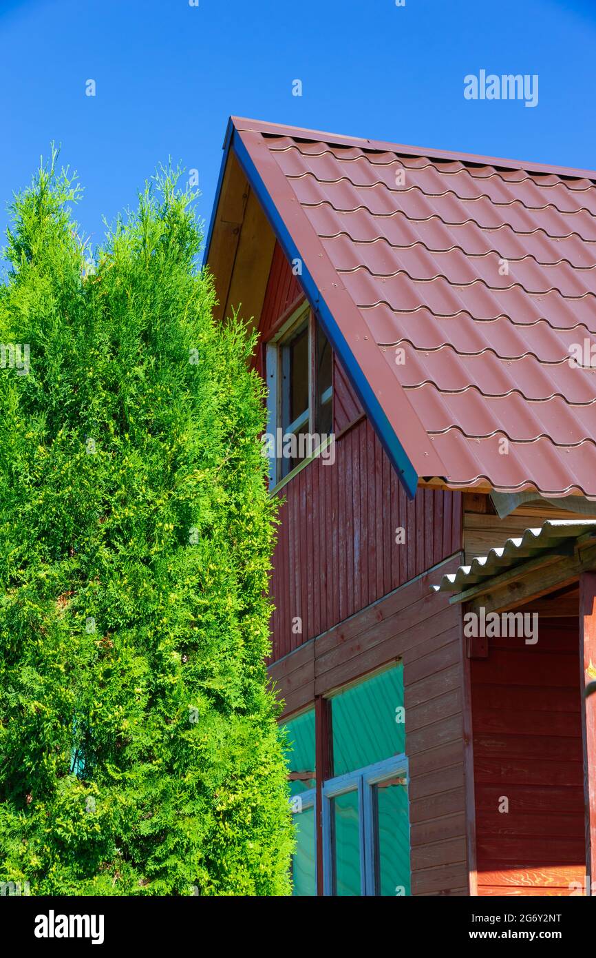Old wooden red house in the village against the background of blue sky and green foliage. Hot sunny summer day. Medium plan Stock Photo