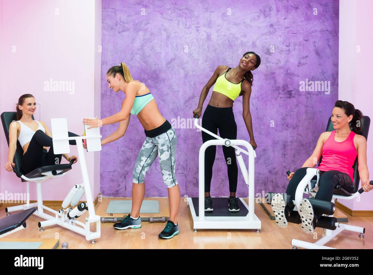Determined fit women wearing cool sport outfits while exercising under the guidance of an experienced fitness instructor at a health club with modern Stock Photo