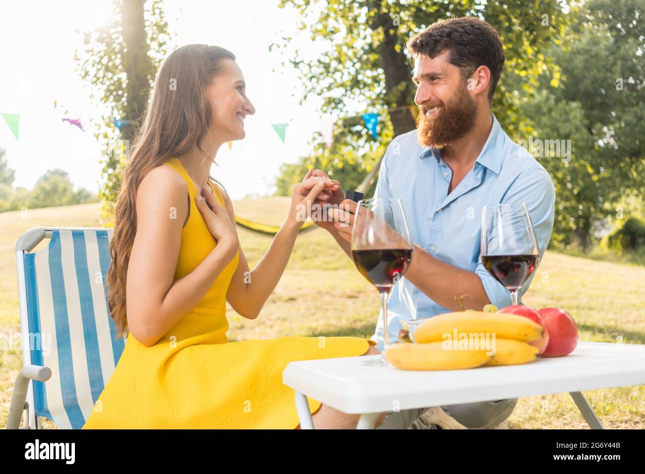 Beautiful young woman accepting with joy and emotion the marriage proposal from her boyfriend during romantic picnic in a sunny day of summer Stock Photo