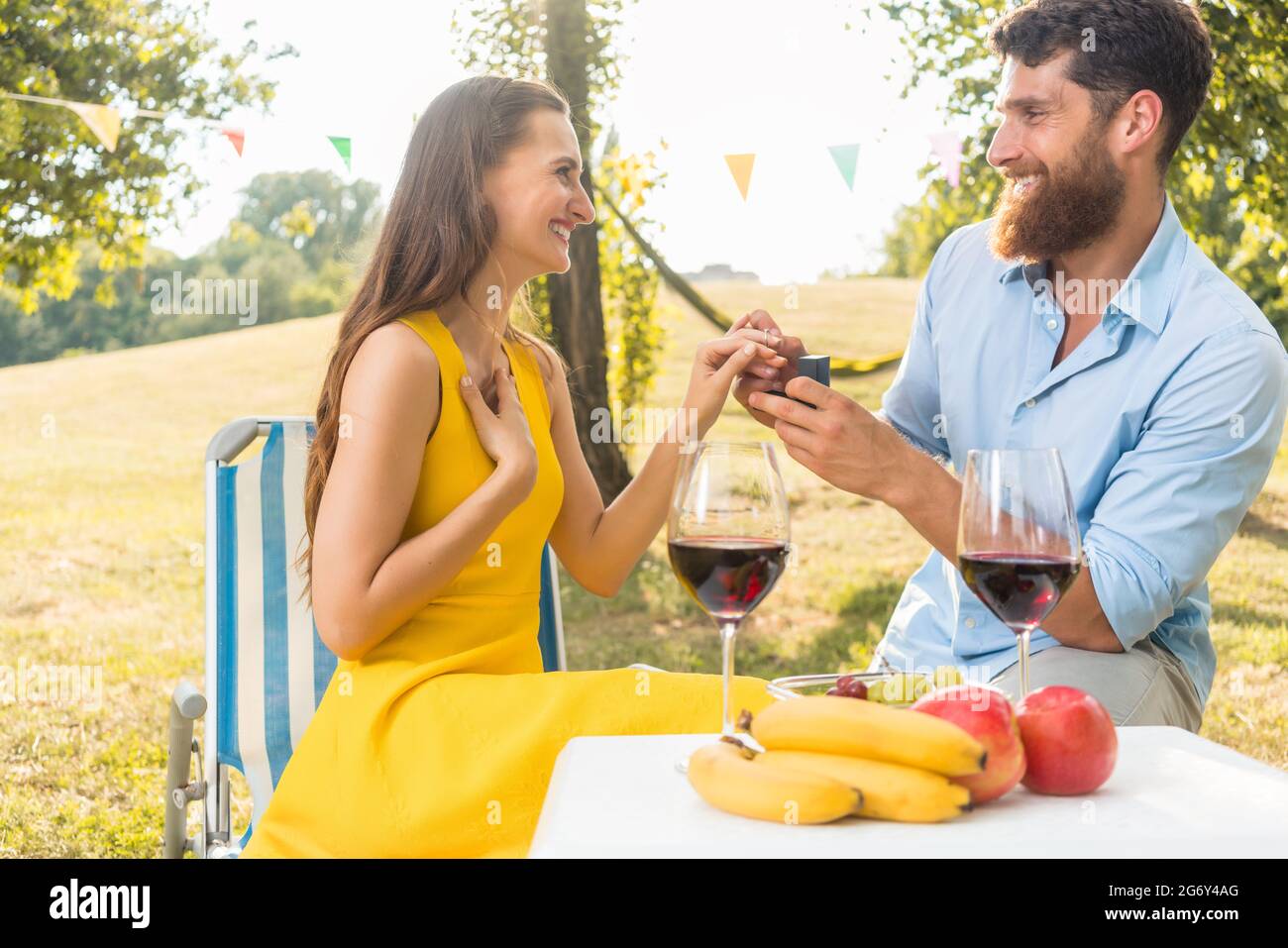 Beautiful young woman accepting with joy and emotion the marriage proposal from her boyfriend during romantic picnic in a sunny day of summer Stock Photo