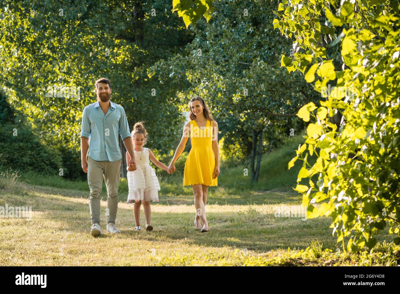Beautiful caring parents holding the hands of their lovely daughter while walking together outdoors in the park in a perfect day of summer Stock Photo