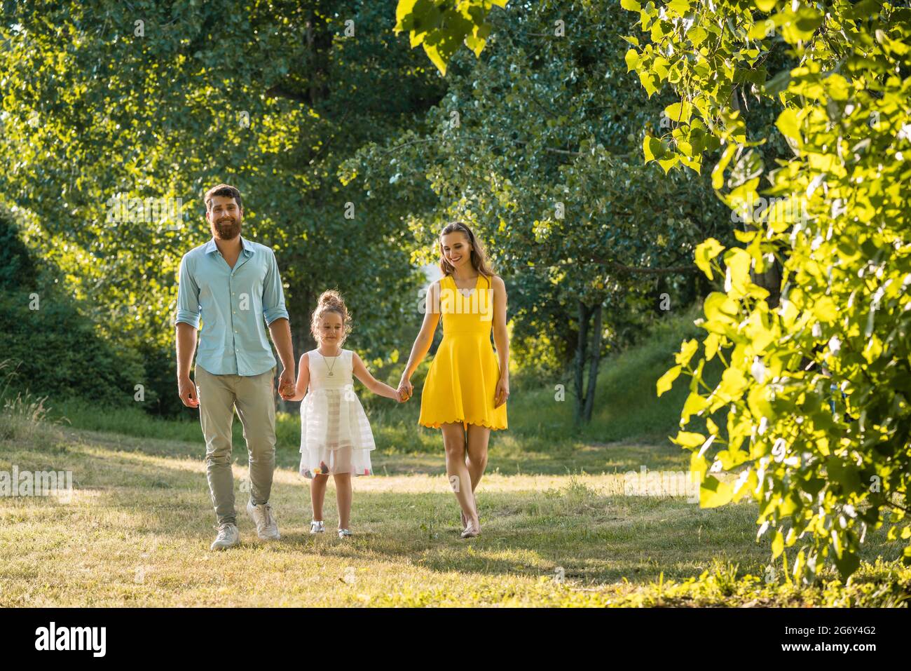 Beautiful caring parents holding the hands of their lovely daughter while walking together outdoors in the park in a perfect day of summer Stock Photo