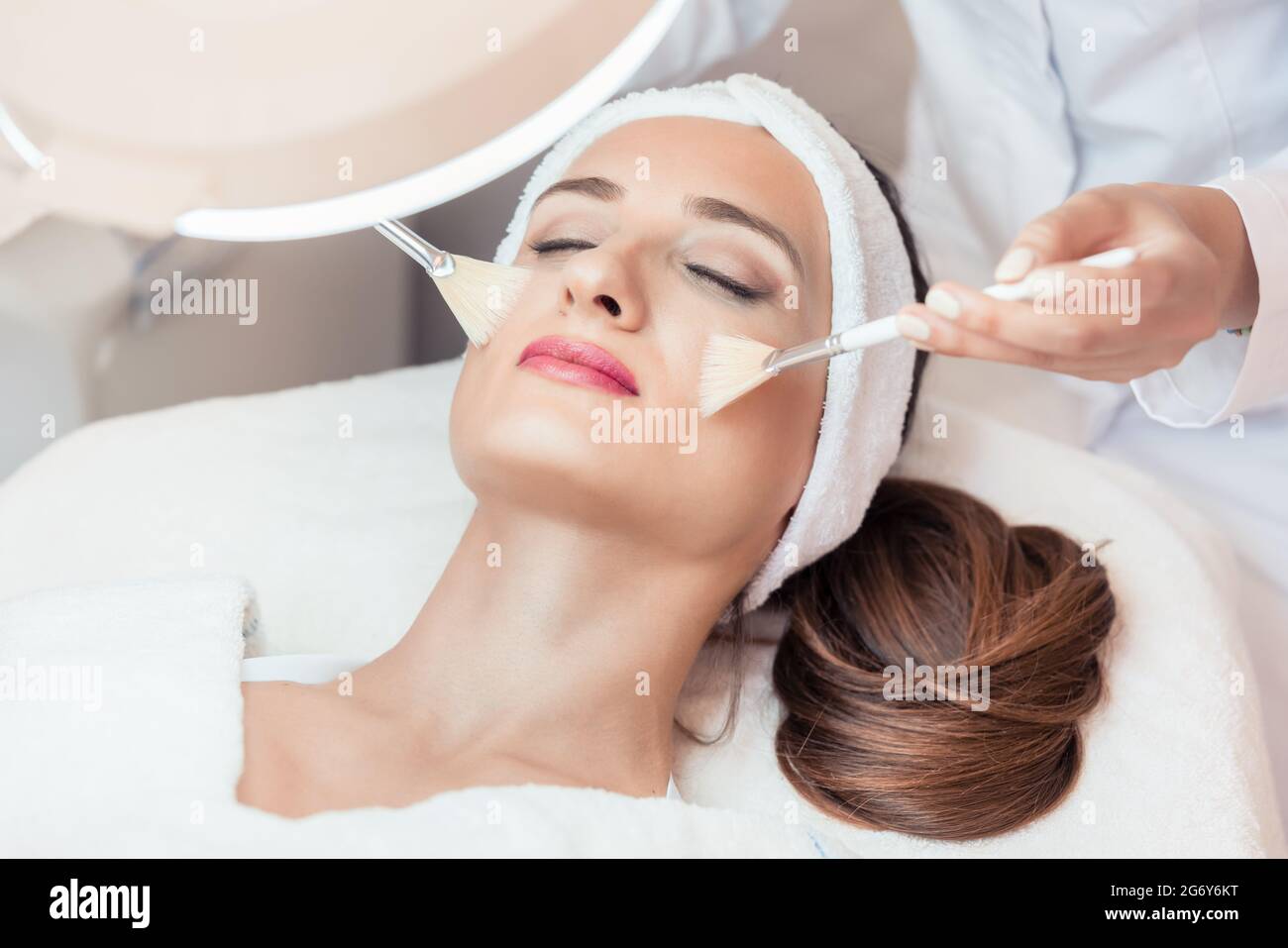 High-angle close-up view of the face of a beautiful woman during anti-aging facial massage with soft brushes in a modern cosmetic center Stock Photo