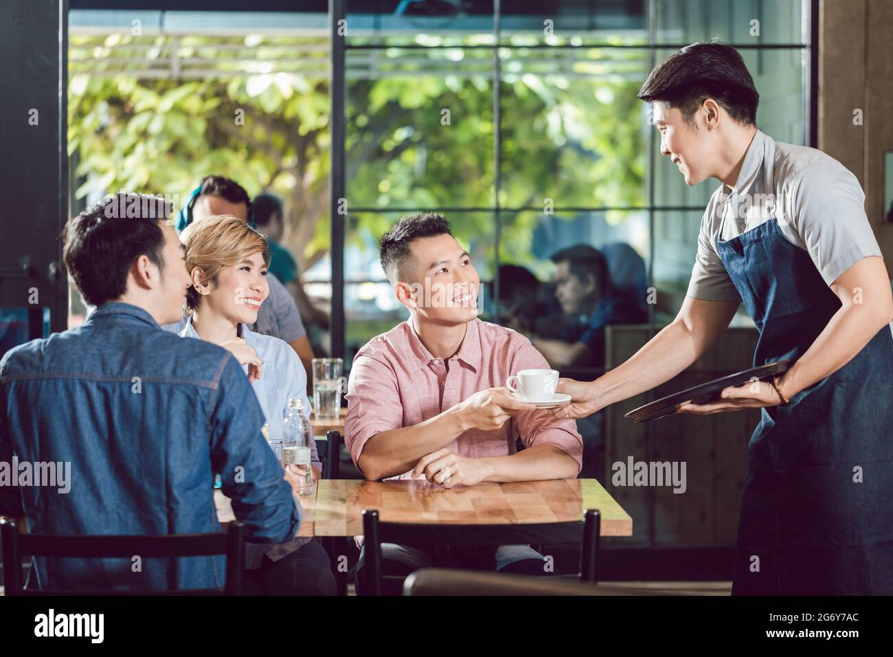 Happy male waiter serving coffee to the customer in the coffee shop