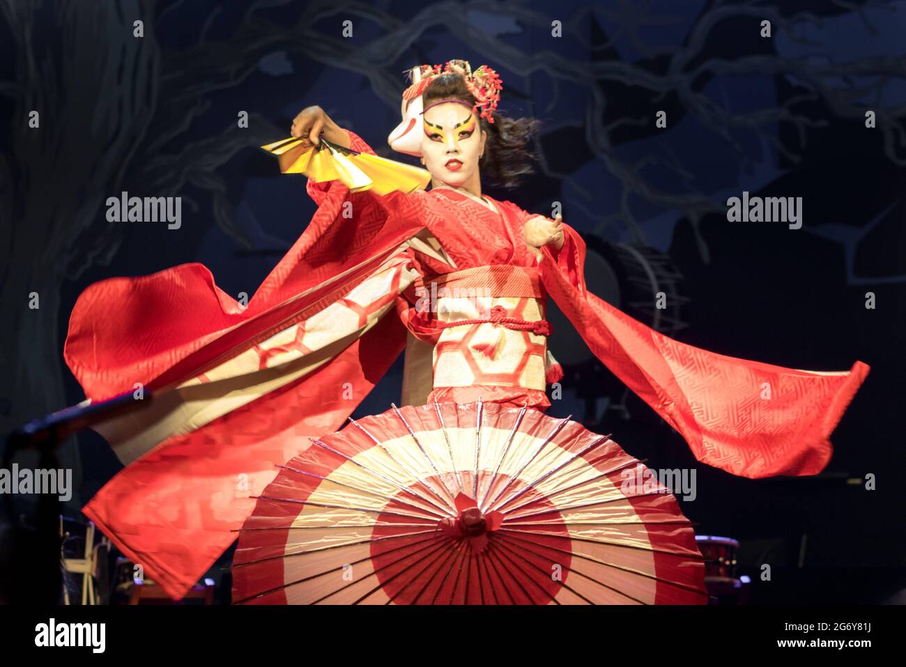 Woman dances with a fan and umbrella, with flowing sleeves. Traditional Japanese performance red fox dance. Kino Kitsune fox is a character in Japanes Stock Photo