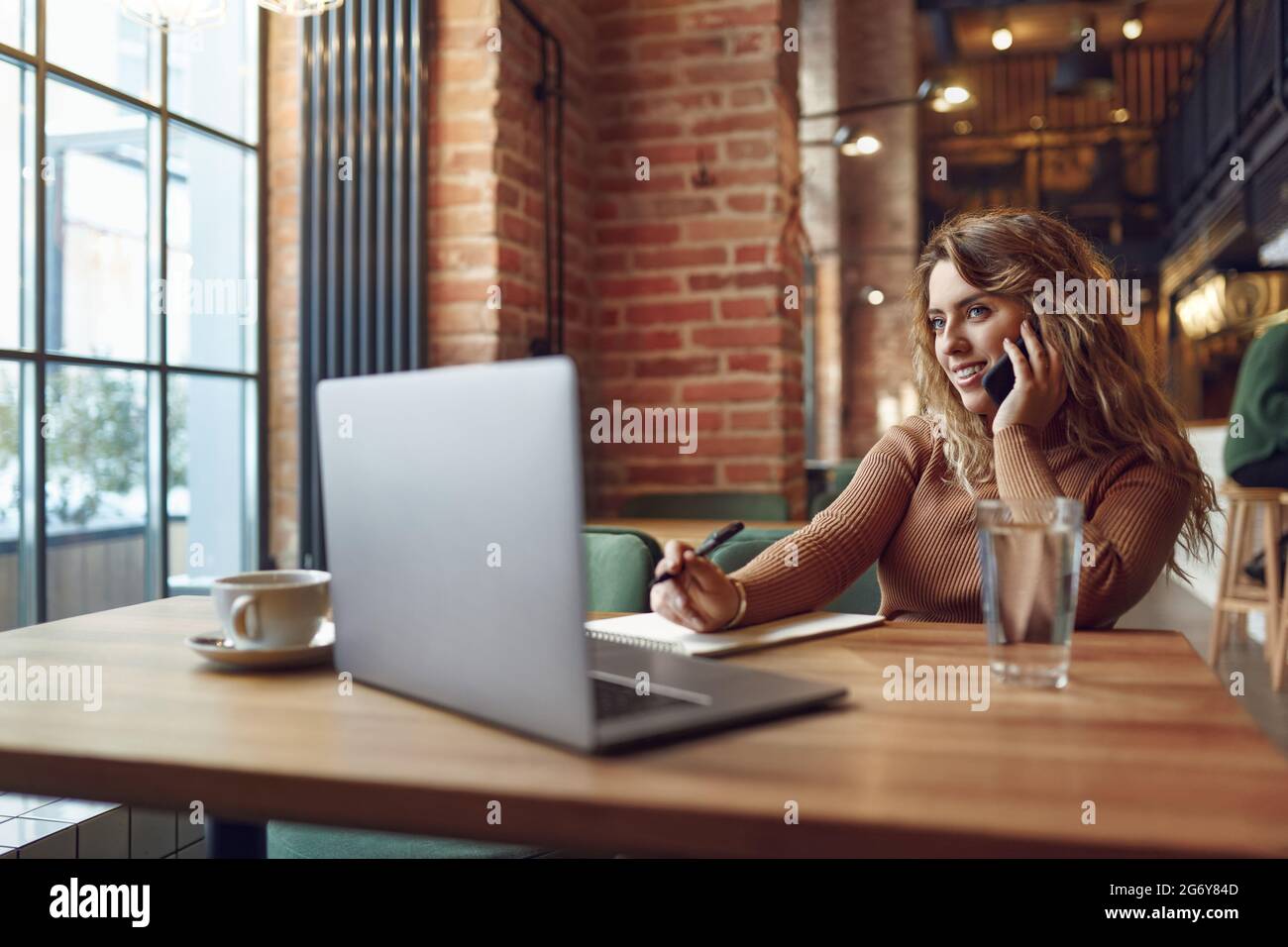 Pretty woman taking notes while talking on mobile Stock Photo