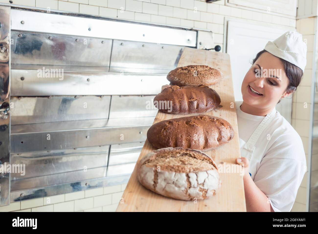 A baker woman holds fresh bread in her hand against the background of bakers  working in a bakery Stock Photo - Alamy