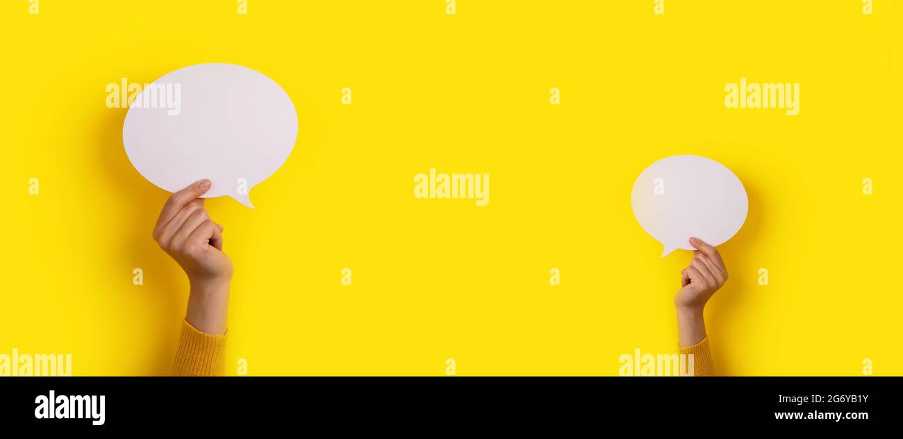 hands holding dialogue icon over yellow background, panoramic mock-up image Stock Photo