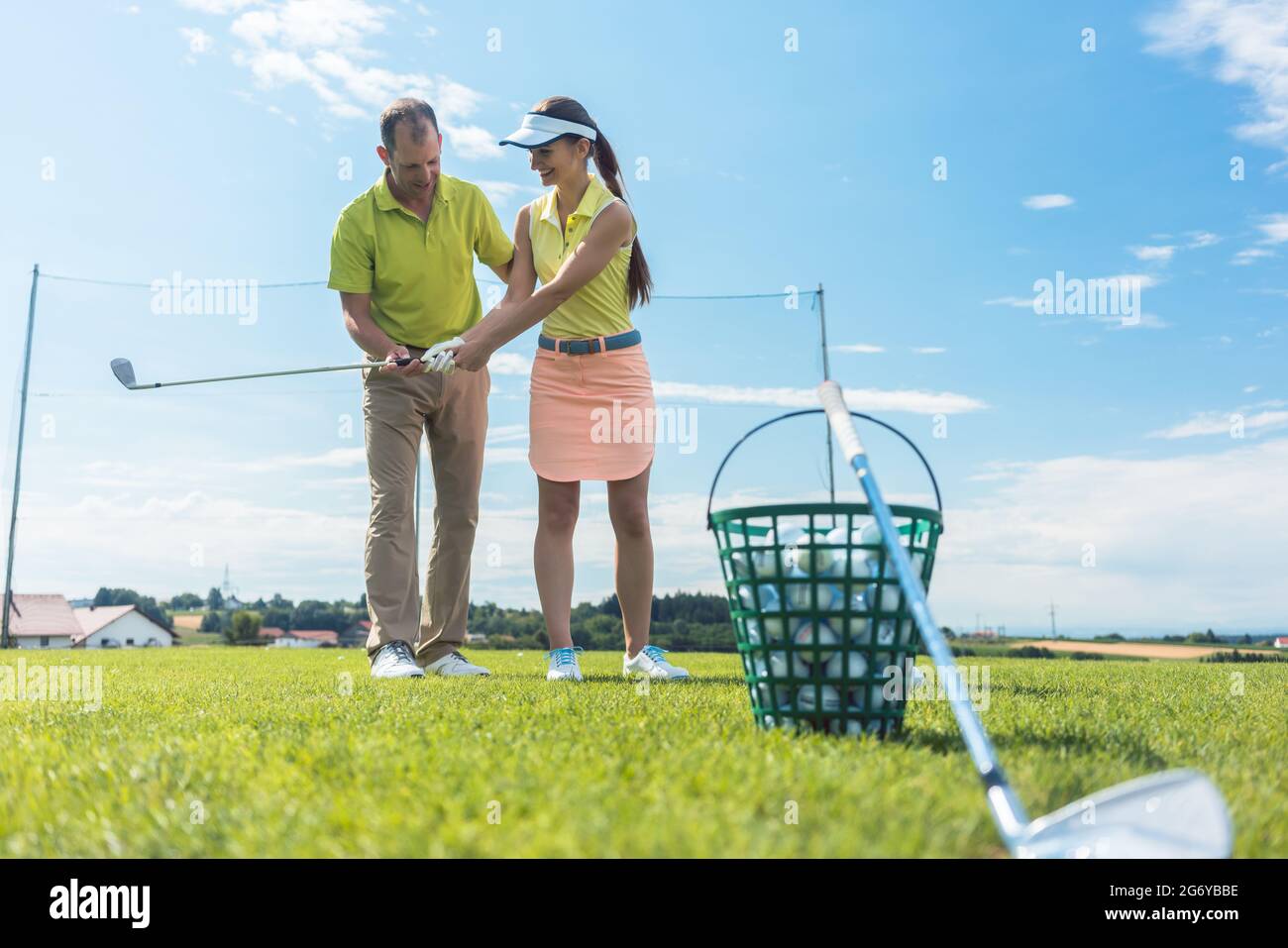 Full length of a cheerful young woman learning the correct grip and move for using the iron golf club, under the guidance of a skilled male teacher ou Stock Photo