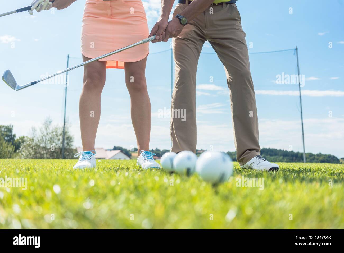 Low section of man and woman holding iron clubs, while practicing together the correct grip and move for playing golf on the green grass of a professi Stock Photo